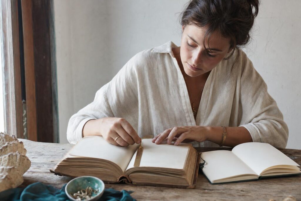 Junge Frau vergleicht an einem Holztisch ein geöffnetes Buch mit ihren Notizen; ein Messing-Lesezeichen trennt die Textabschnitte.