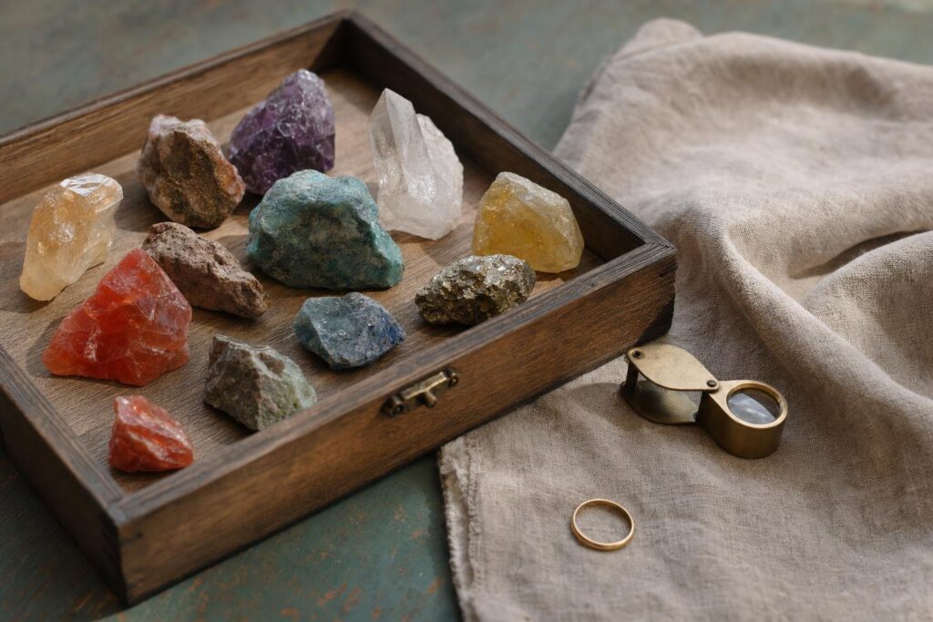 Natürliche Chakra-Steine in einem Holzkasten neben Leinen, Lupe und einem kleinen Messingring