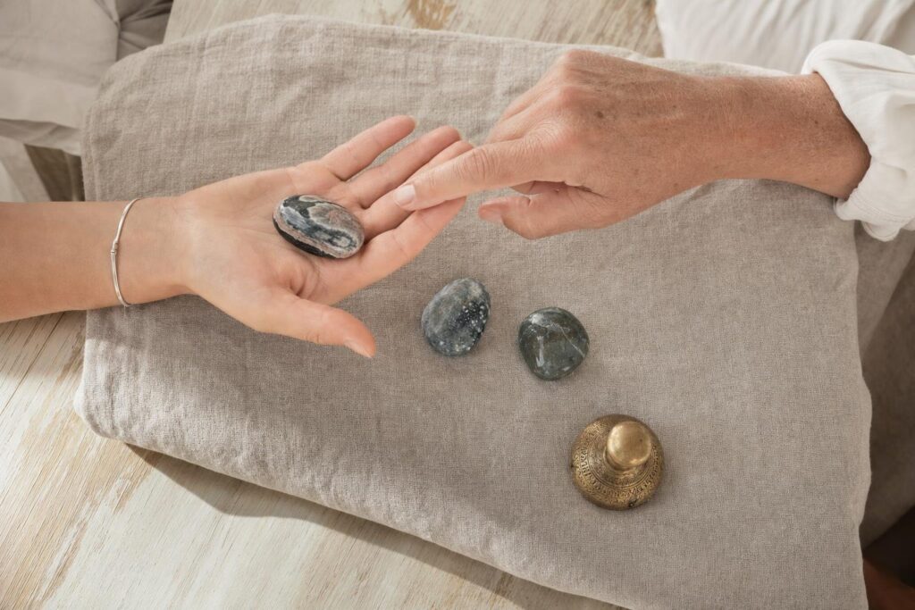 Zwei erwachsene Hände vergleichen Form, Farbe und Oberfläche verschiedener Chakrasteine