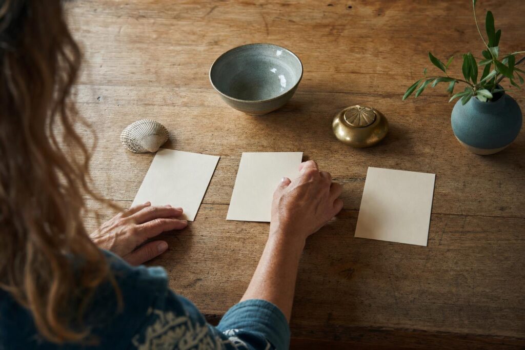 Hände ordnen drei leere Papierkarten mit Muschel, Schale und Zweig für eine Abschlussübung