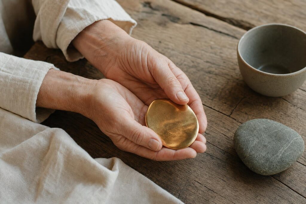Ältere Hände halten ein kleines unregelmäßiges goldfarbenes Erinnerungsstück.