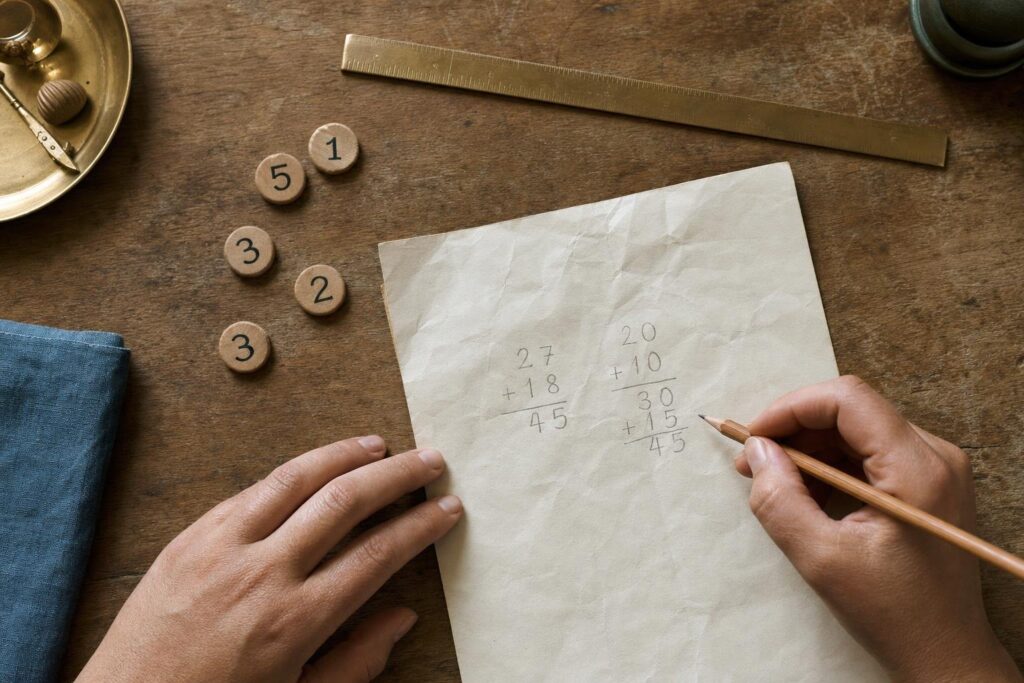Hände addieren die Ziffern eines Beispieldatums auf Papier und vergleichen zwei Reduktionswege.